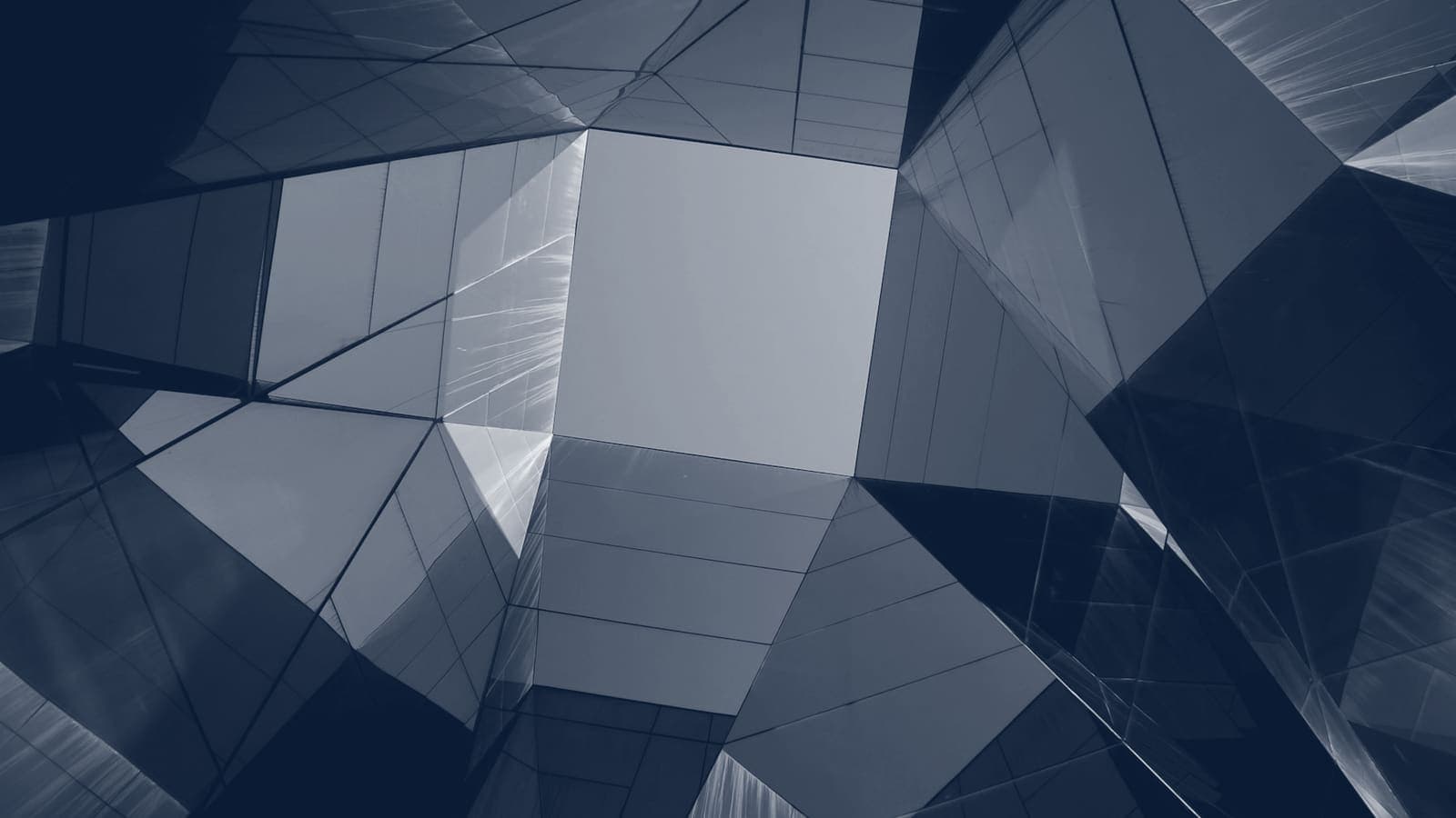Faceted glass facade of a modern building seen from below, panes meeting at sharp angles