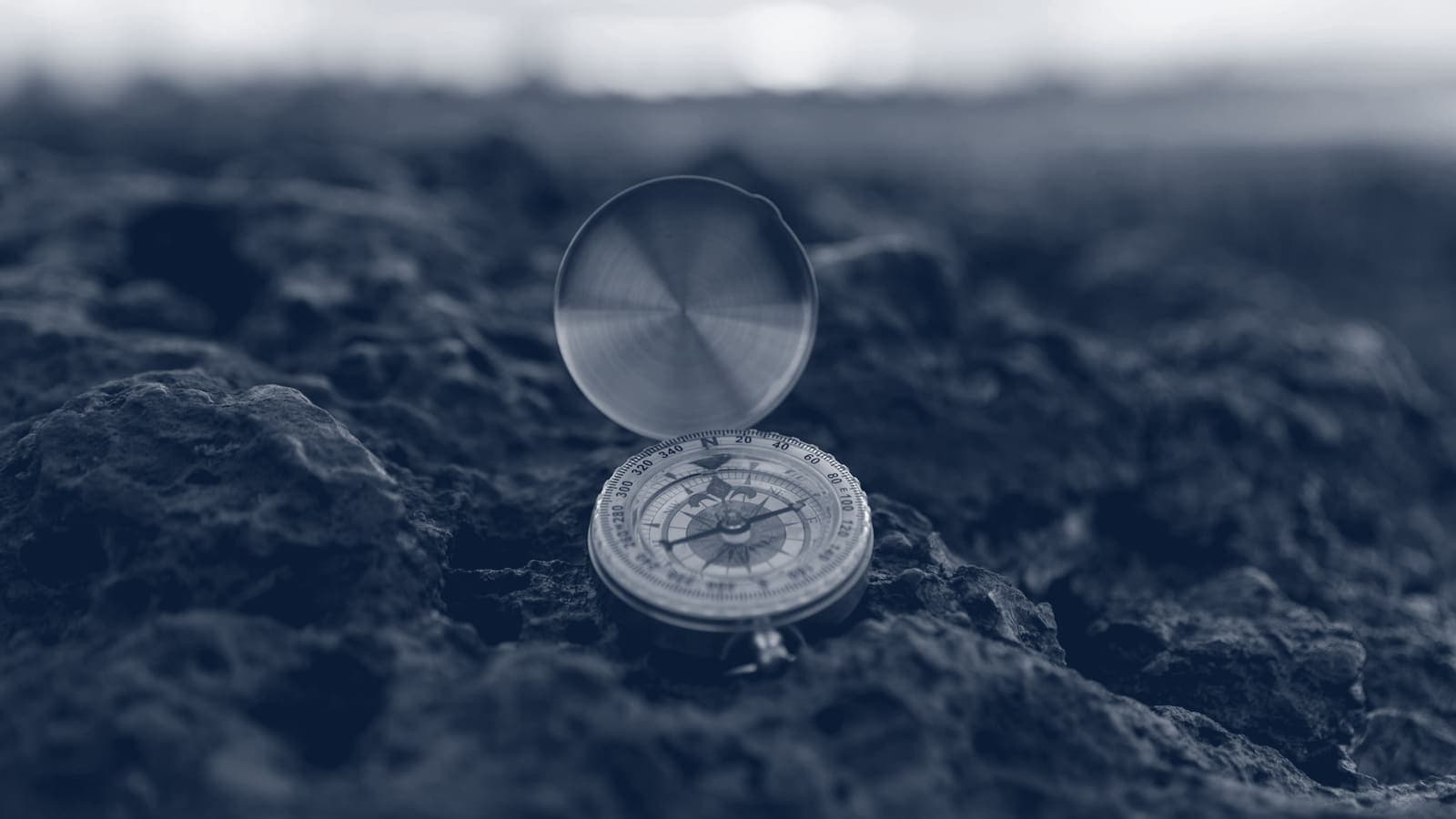 Open pocket compass standing on rough rock with a blurred horizon behind