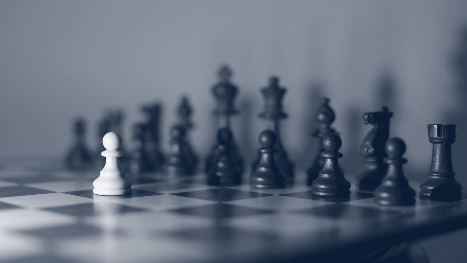 Single white pawn on a chessboard facing a row of dark pieces