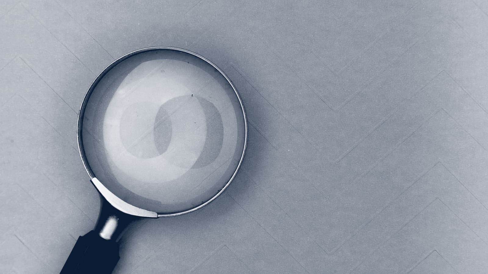 Magnifying glass with a dark handle lying on a plain, empty surface